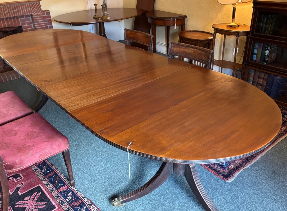 A large polished Regency design mahogany dining table featuring a triple pedestal base with inlaid edge details and brass castors. View VII