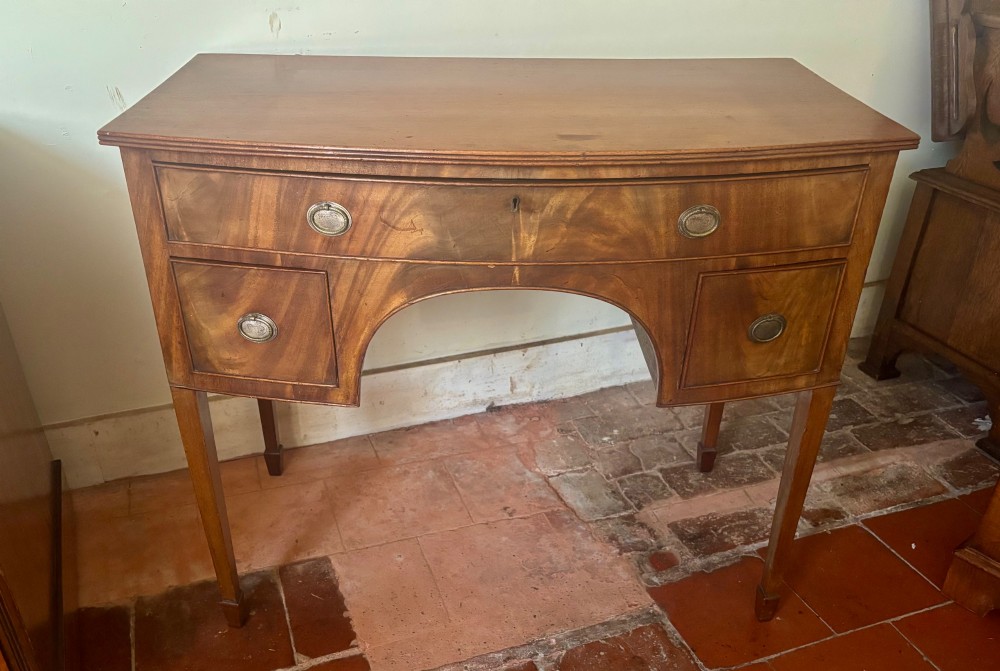 A Regency mahogany bow-front dressing table with a central arched kneehole, three drawers with oval brass handles, and square tapered legs. View V