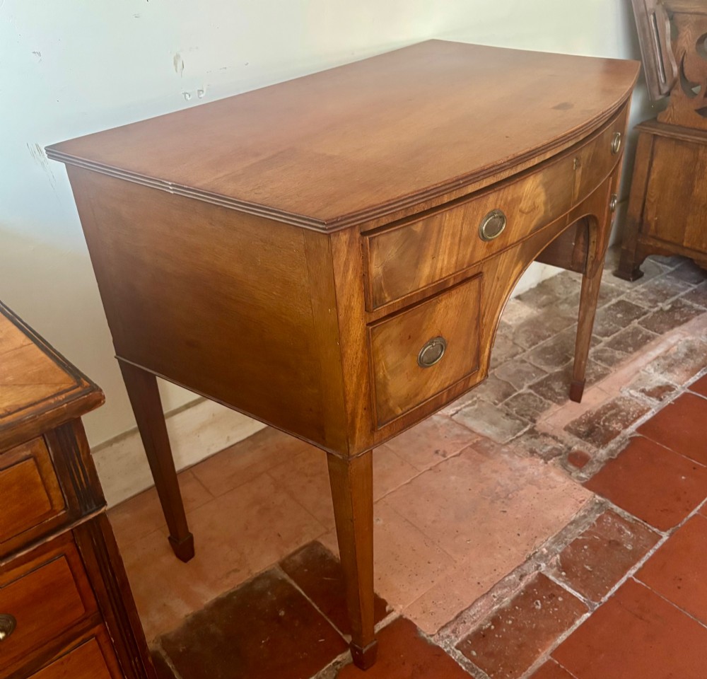 A Regency mahogany bow-front dressing table with a central arched kneehole, three drawers with oval brass handles, and square tapered legs. View VI