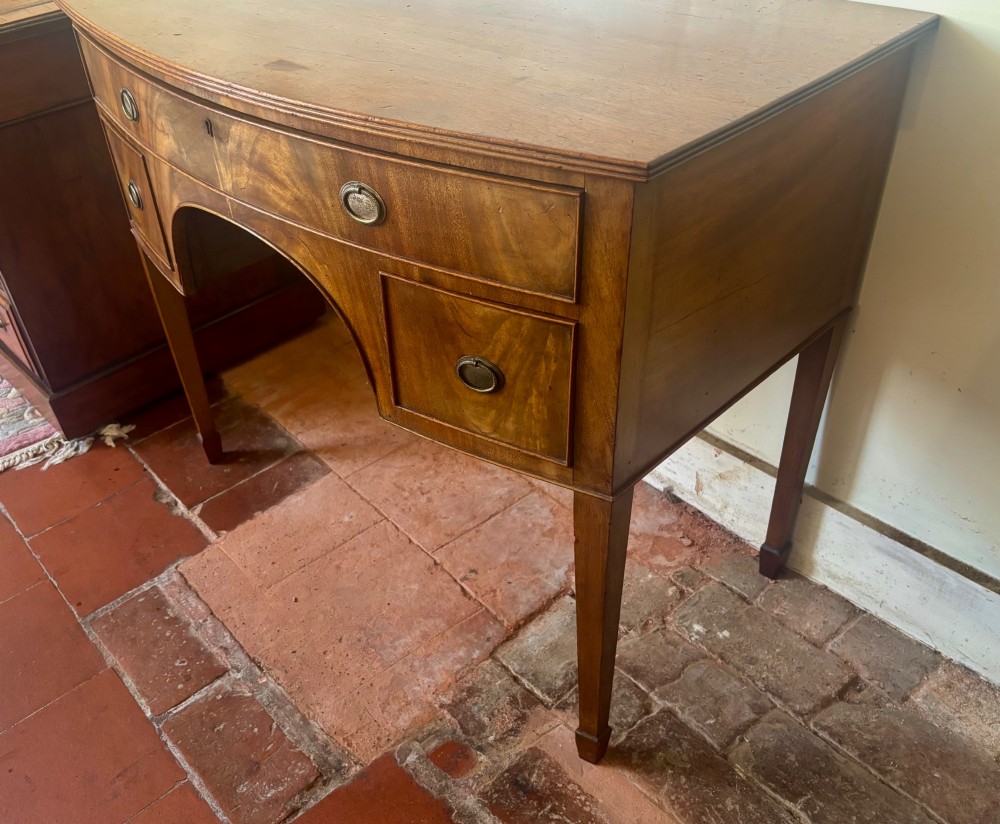 A Regency mahogany bow-front dressing table with a central arched kneehole, three drawers with oval brass handles, and square tapered legs. View VII