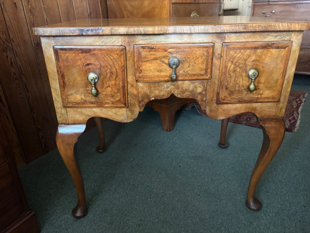 A Georgian style burr walnut lowboy featuring three drawers with brass drop handles, a shaped apron, and cabriole legs. View V