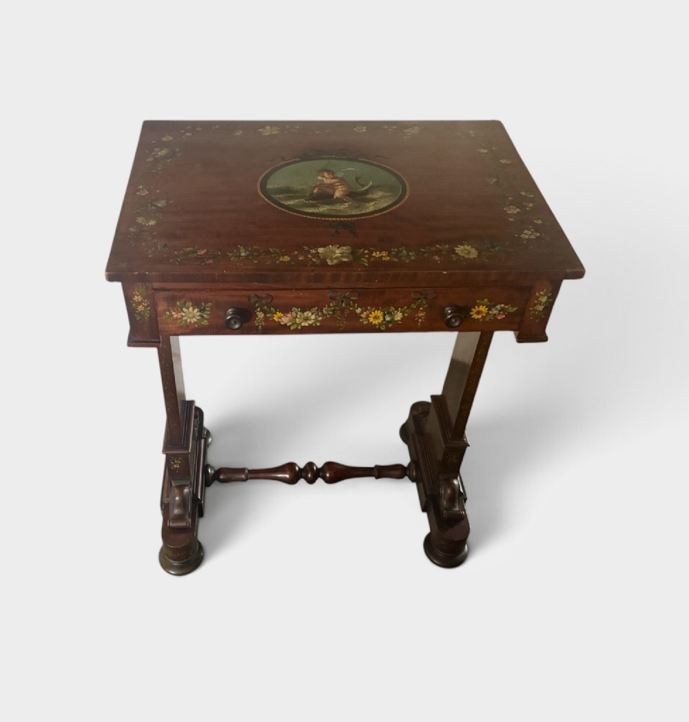 An early Victorian mahogany side table featuring hand-painted floral garlands across the surface and drawer, supported by trestle legs and a turned central stretcher.