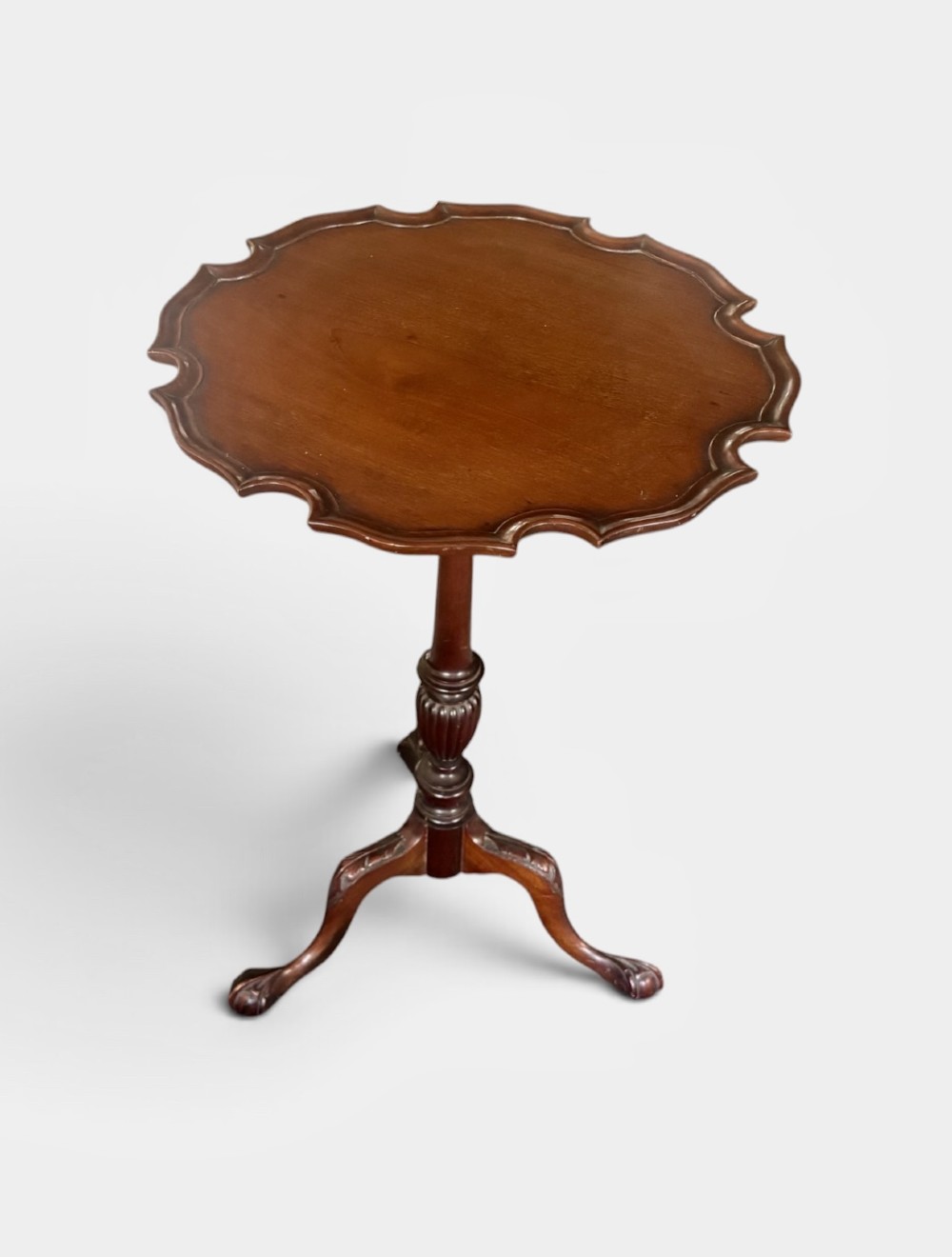 A small mahogany tripod table featuring a raised scalloped piecrust top supported by a carved central pedestal and three cabriole legs.
