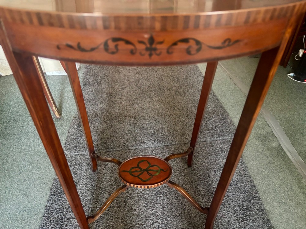 An oval Edwardian satinwood occasional table featuring hand-painted floral garlands, a central classical portrait medallion, and tapered legs linked by a circular stretcher undertier. View VI