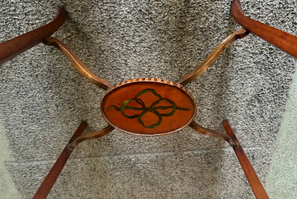 An oval Edwardian satinwood occasional table featuring hand-painted floral garlands, a central classical portrait medallion, and tapered legs linked by a circular stretcher undertier. View VII