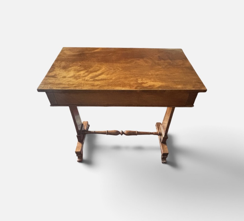 An English Regency mahogany writing table with a polished rectangular top, trestle side supports, turned central stretcher, and carved feet. View II