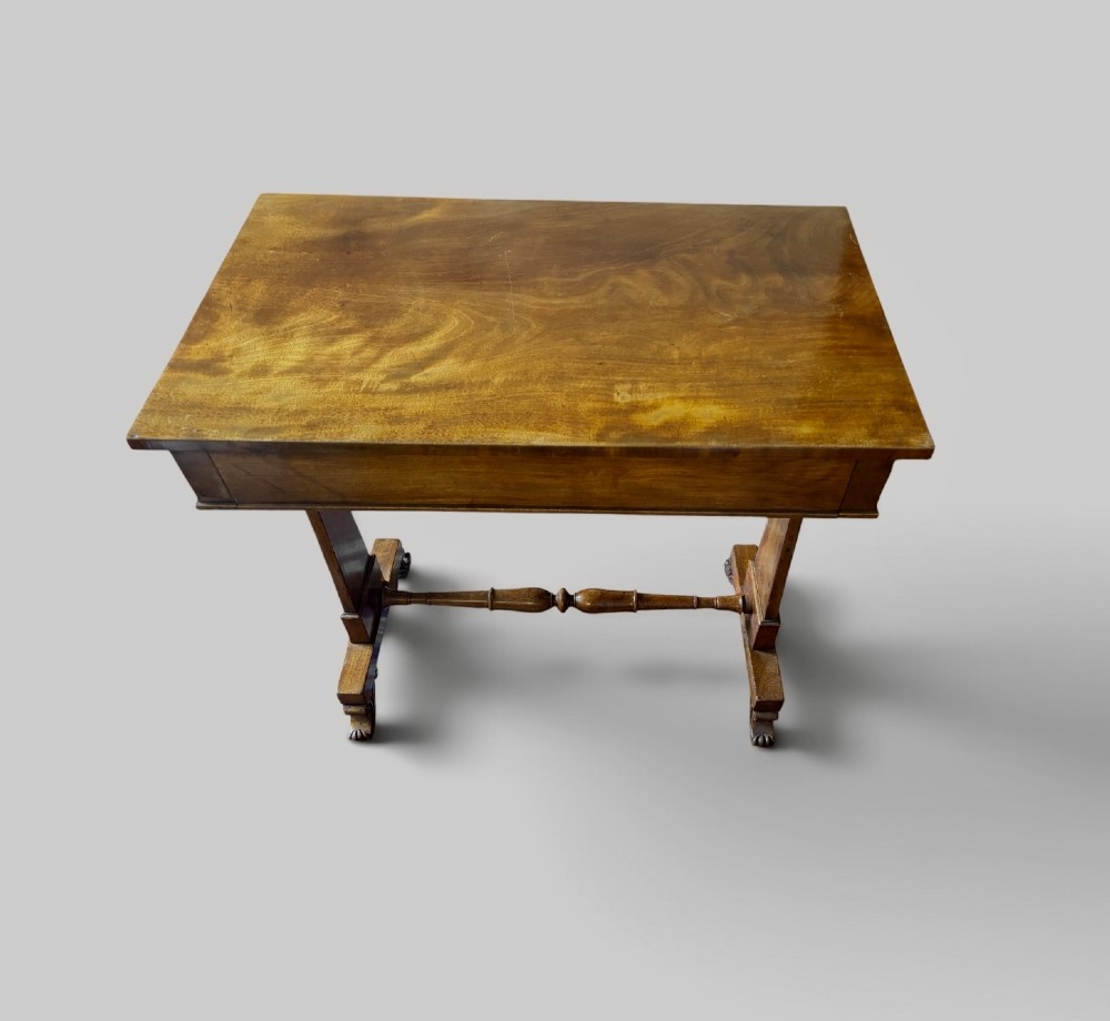 An English Regency mahogany writing table with a polished rectangular top, trestle side supports, turned central stretcher, and carved feet. View III