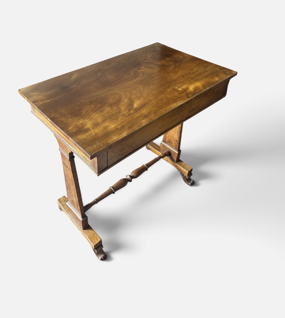 An English Regency mahogany writing table with a polished rectangular top, trestle side supports, turned central stretcher, and carved feet. View IV