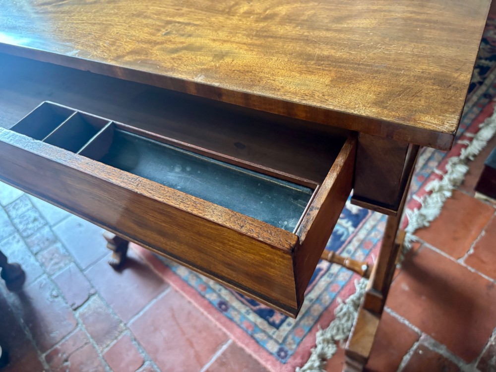 An English Regency mahogany writing table with a polished rectangular top, trestle side supports, turned central stretcher, and carved feet. View VII