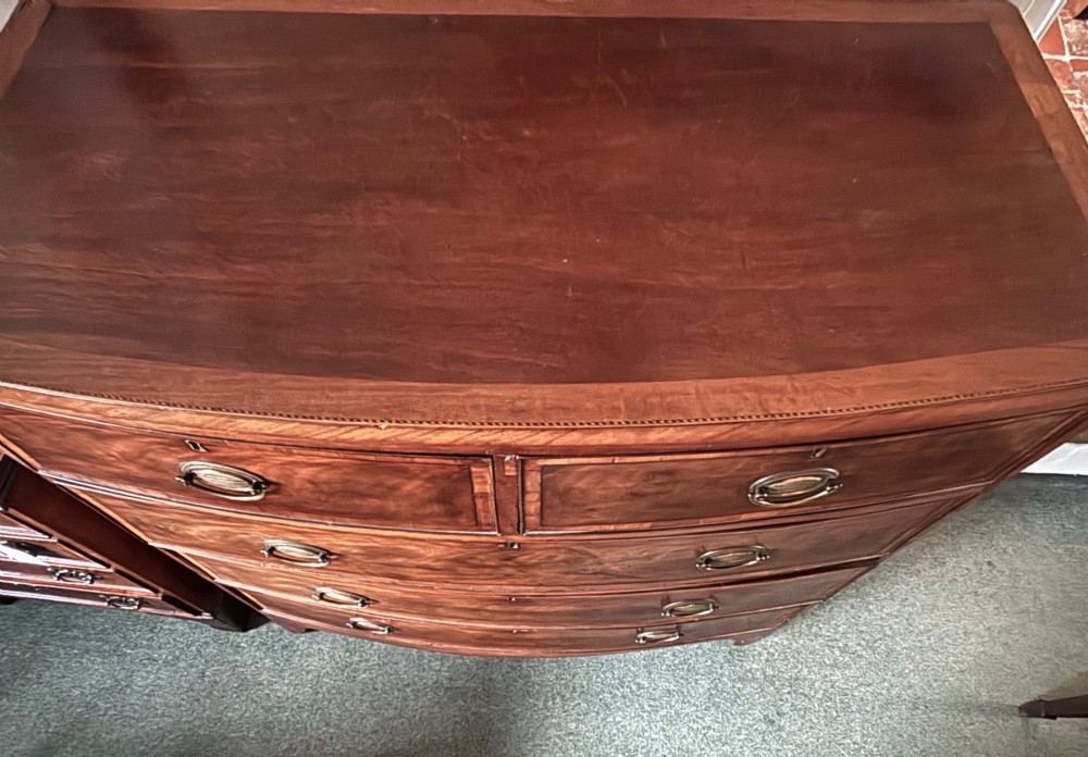 A Regency mahogany bowfront chest of drawers featuring two short over three long graduated drawers with satinwood crossbanding and brass oval plate handles. View II