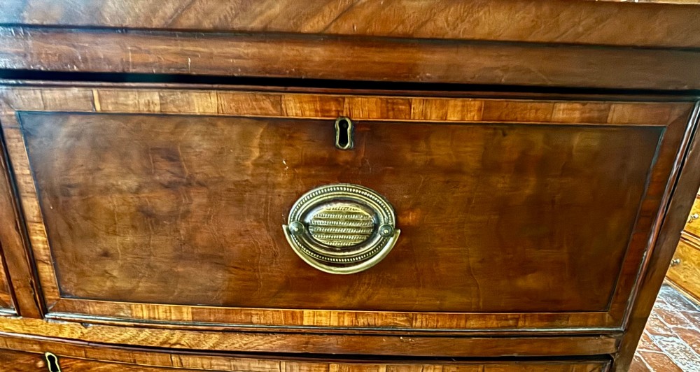A Regency mahogany bowfront chest of drawers featuring two short over three long graduated drawers with satinwood crossbanding and brass oval plate handles. View VI