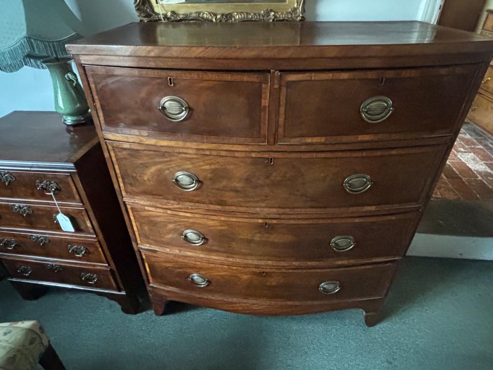 A Regency mahogany bowfront chest of drawers featuring two short over three long graduated drawers with satinwood crossbanding and brass oval plate handles. View VIII