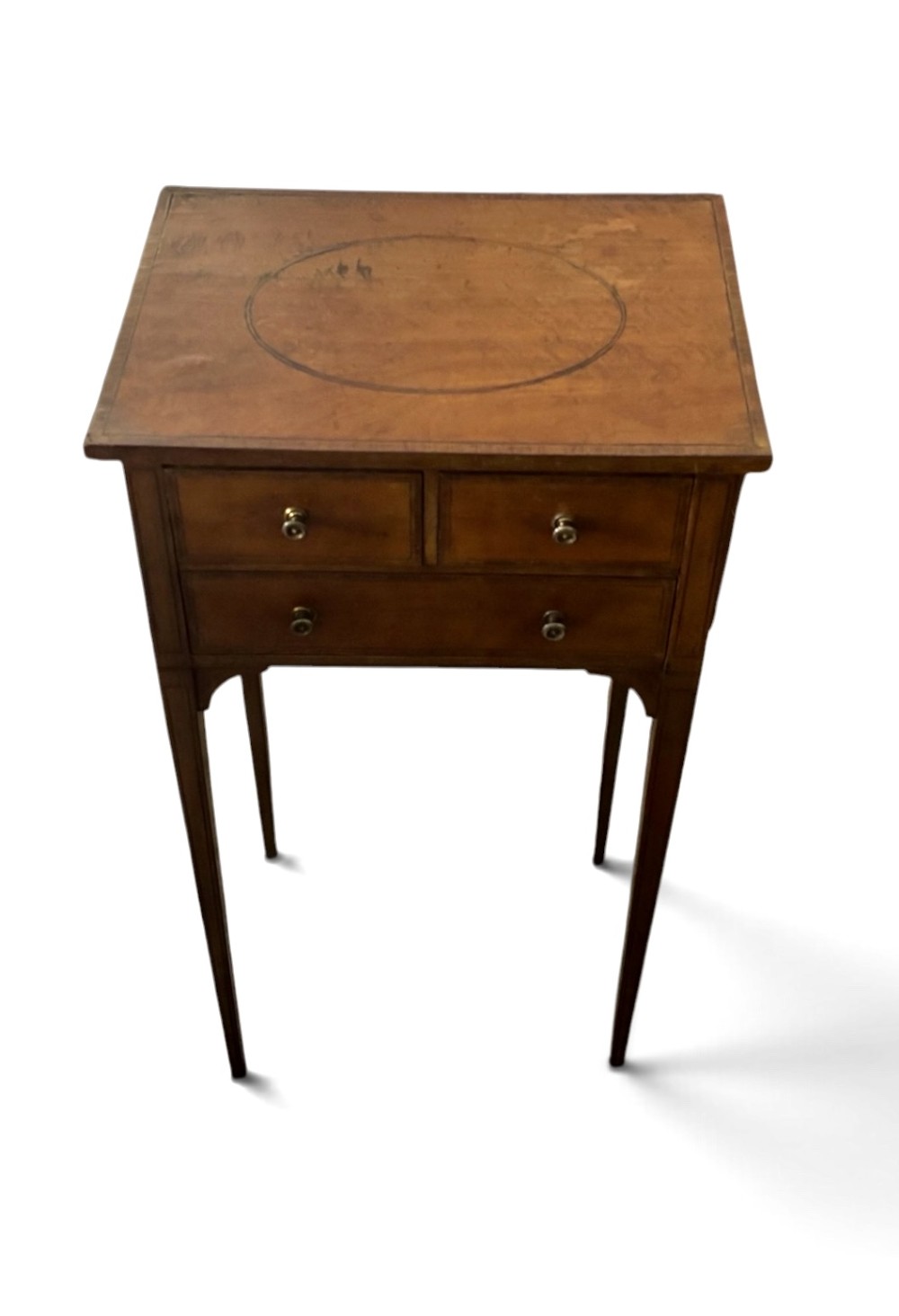 An early nineteenth-century satinwood side table featuring an oval inlaid top panel, three drawers with brass knob handles, and slender tapered square legs. View II