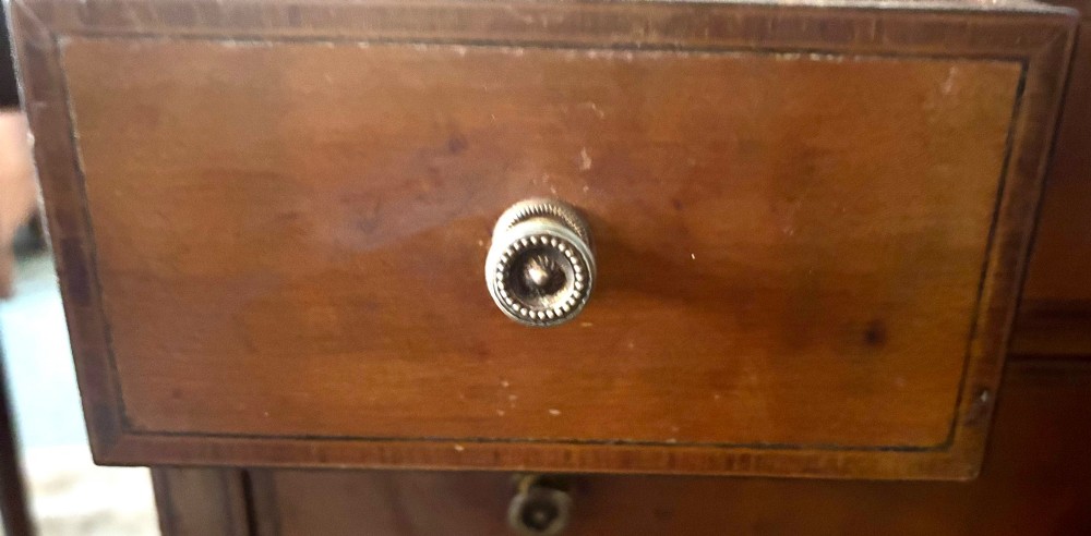 An early nineteenth-century satinwood side table featuring an oval inlaid top panel, three drawers with brass knob handles, and slender tapered square legs. View VI