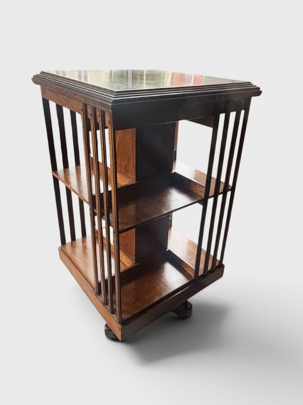 An Edwardian walnut revolving bookcase featuring two tiers of open shelving, vertical slatted sides, and a moulded top edge.