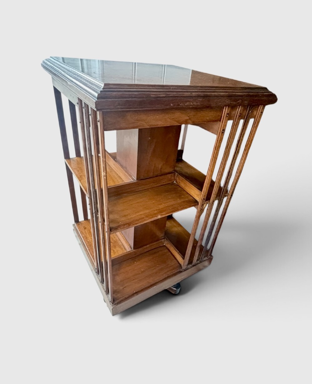 An Edwardian walnut revolving bookcase featuring two tiers of open shelving, vertical slatted sides, and a moulded top edge. View III