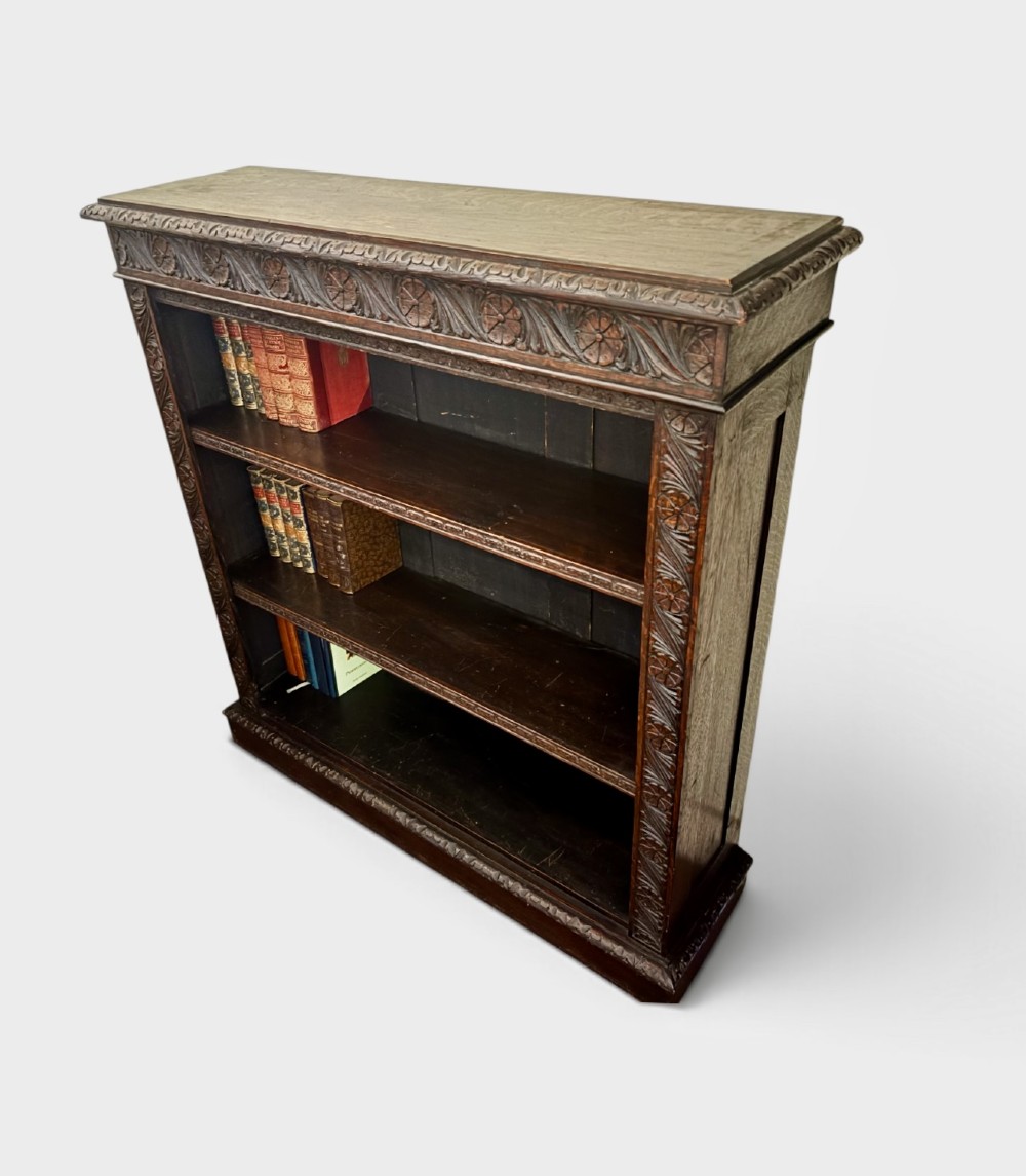 A Victorian dark carved oak open bookcase featuring detailed rosette hand-carvings along the frieze and outer border with three open shelves holding books. View II