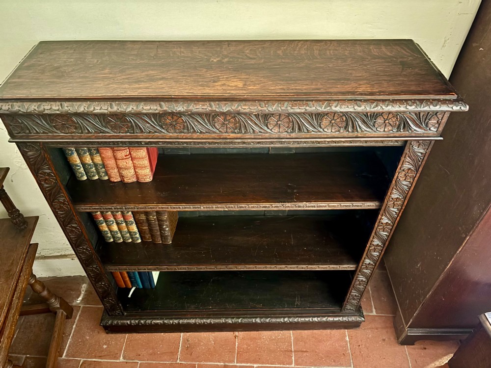 A Victorian dark carved oak open bookcase featuring detailed rosette hand-carvings along the frieze and outer border with three open shelves holding books. View III