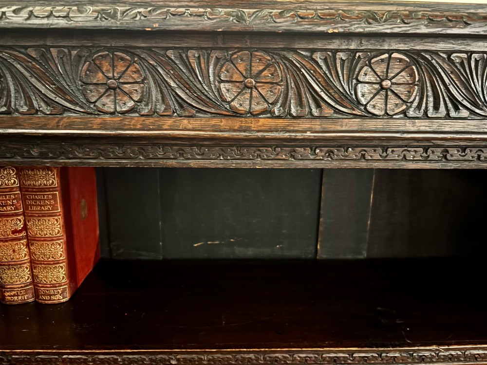 A Victorian dark carved oak open bookcase featuring detailed rosette hand-carvings along the frieze and outer border with three open shelves holding books. View IV