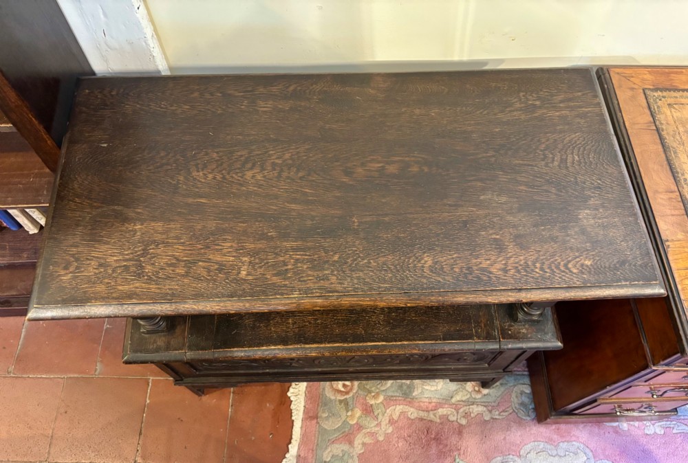 A dark carved oak monks bench featuring a pivoted panel backrest, turned arm supports, and a chest storage base. View IV