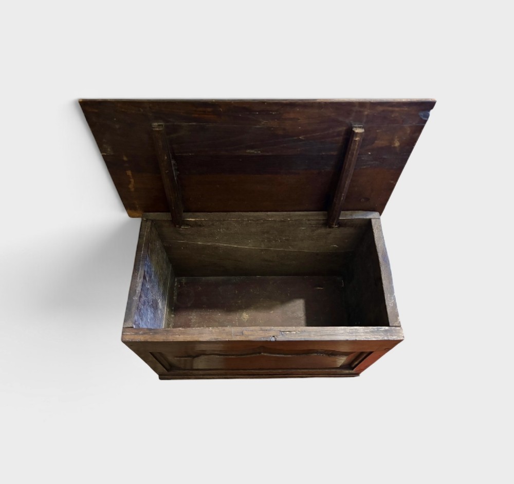 A small dark oak coffer with a hinged rectangular top, shaped fielded front panel, and solid side supports. View II