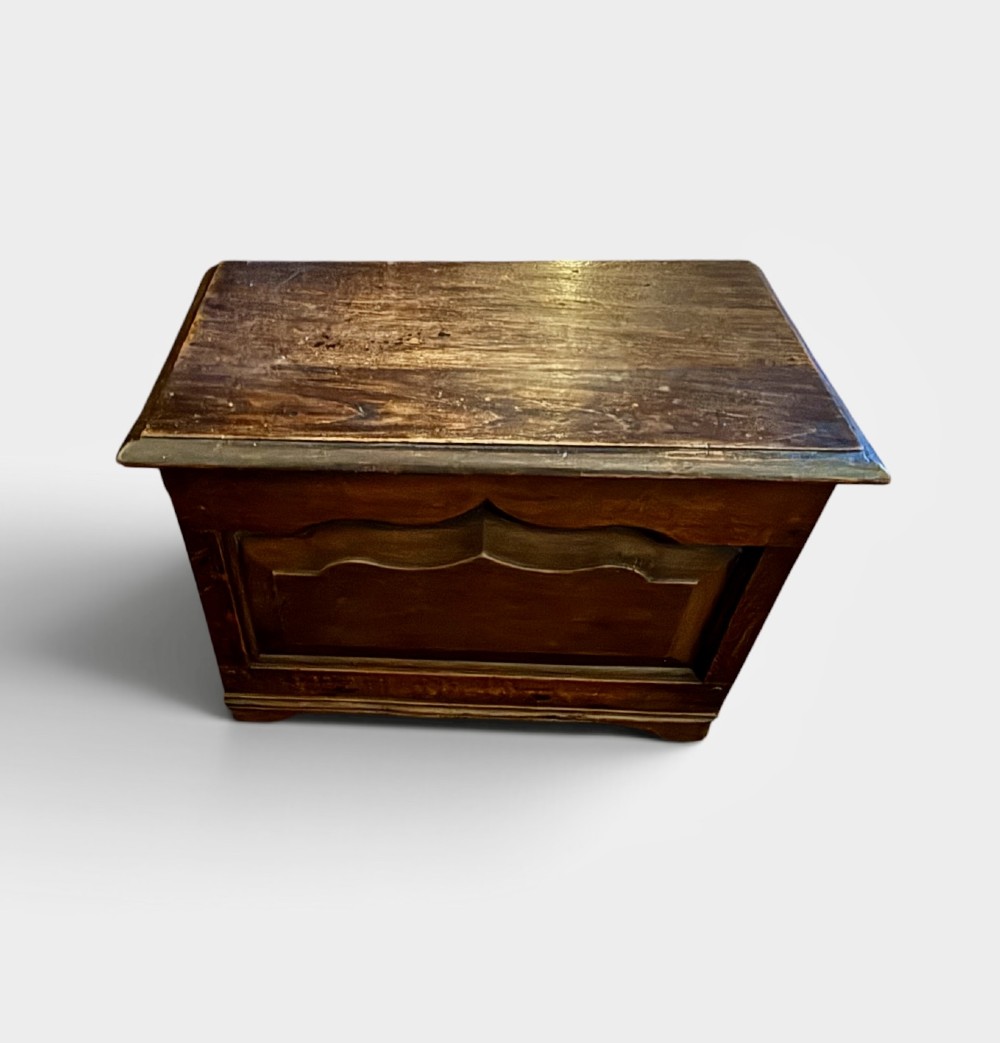 A small dark oak coffer with a hinged rectangular top, shaped fielded front panel, and solid side supports. View IV