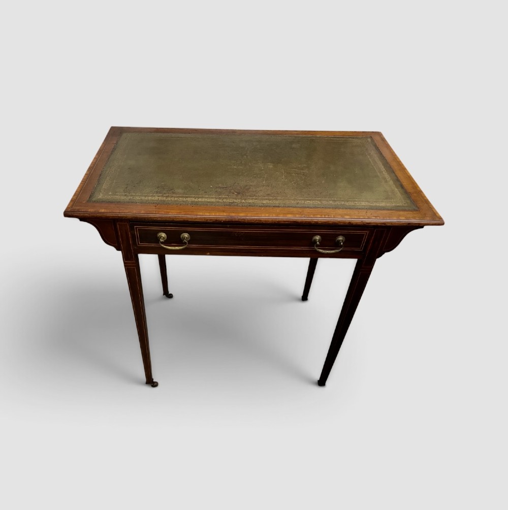 An Edwardian mahogany writing table featuring a green leather insert surface, satinwood crossbanding, one long drawer, and square tapered legs.