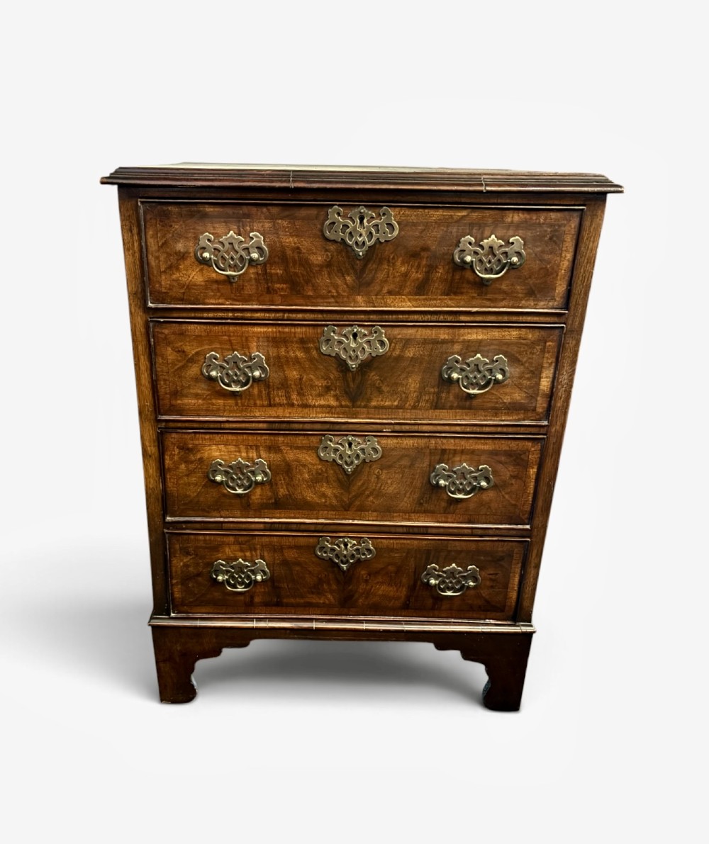 A small 19th-century chest of drawers crafted from figured walnut featuring four graduated drawers, decorative brass handles, and bracket feet.