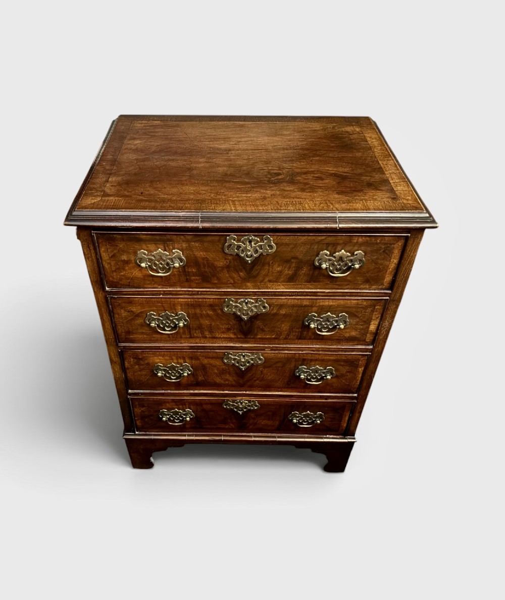 A small 19th-century chest of drawers crafted from figured walnut featuring four graduated drawers, decorative brass handles, and bracket feet. View II
