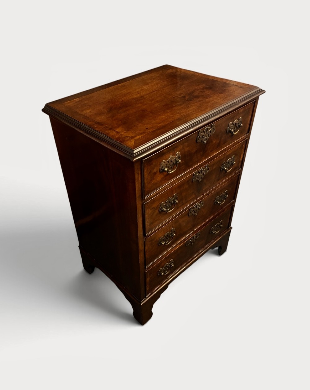A small 19th-century chest of drawers crafted from figured walnut featuring four graduated drawers, decorative brass handles, and bracket feet. View III