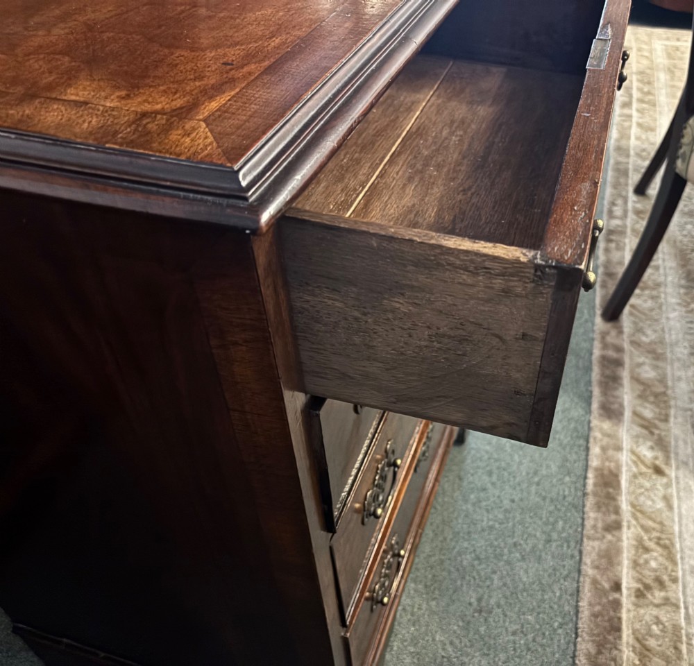 A small 19th-century chest of drawers crafted from figured walnut featuring four graduated drawers, decorative brass handles, and bracket feet. View IV