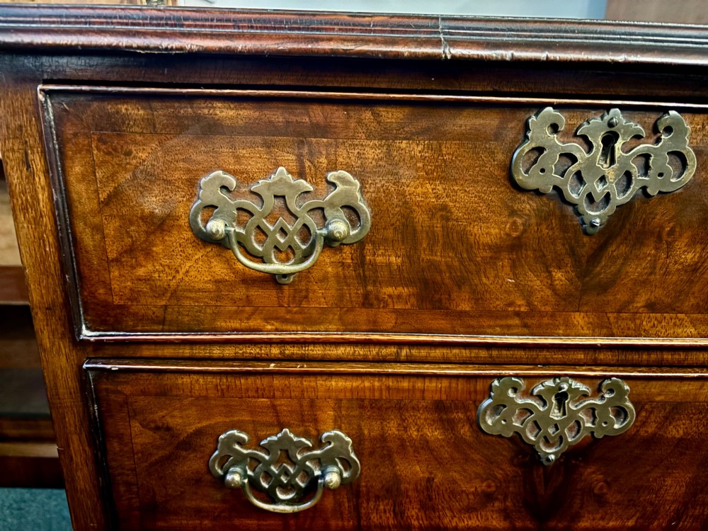 A small 19th-century chest of drawers crafted from figured walnut featuring four graduated drawers, decorative brass handles, and bracket feet. View V