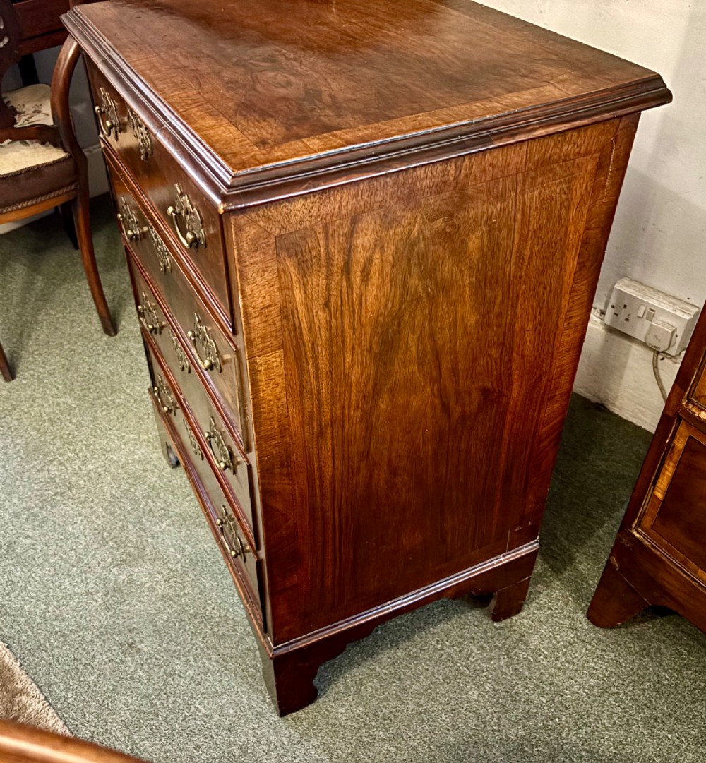 A small 19th-century chest of drawers crafted from figured walnut featuring four graduated drawers, decorative brass handles, and bracket feet. View VI
