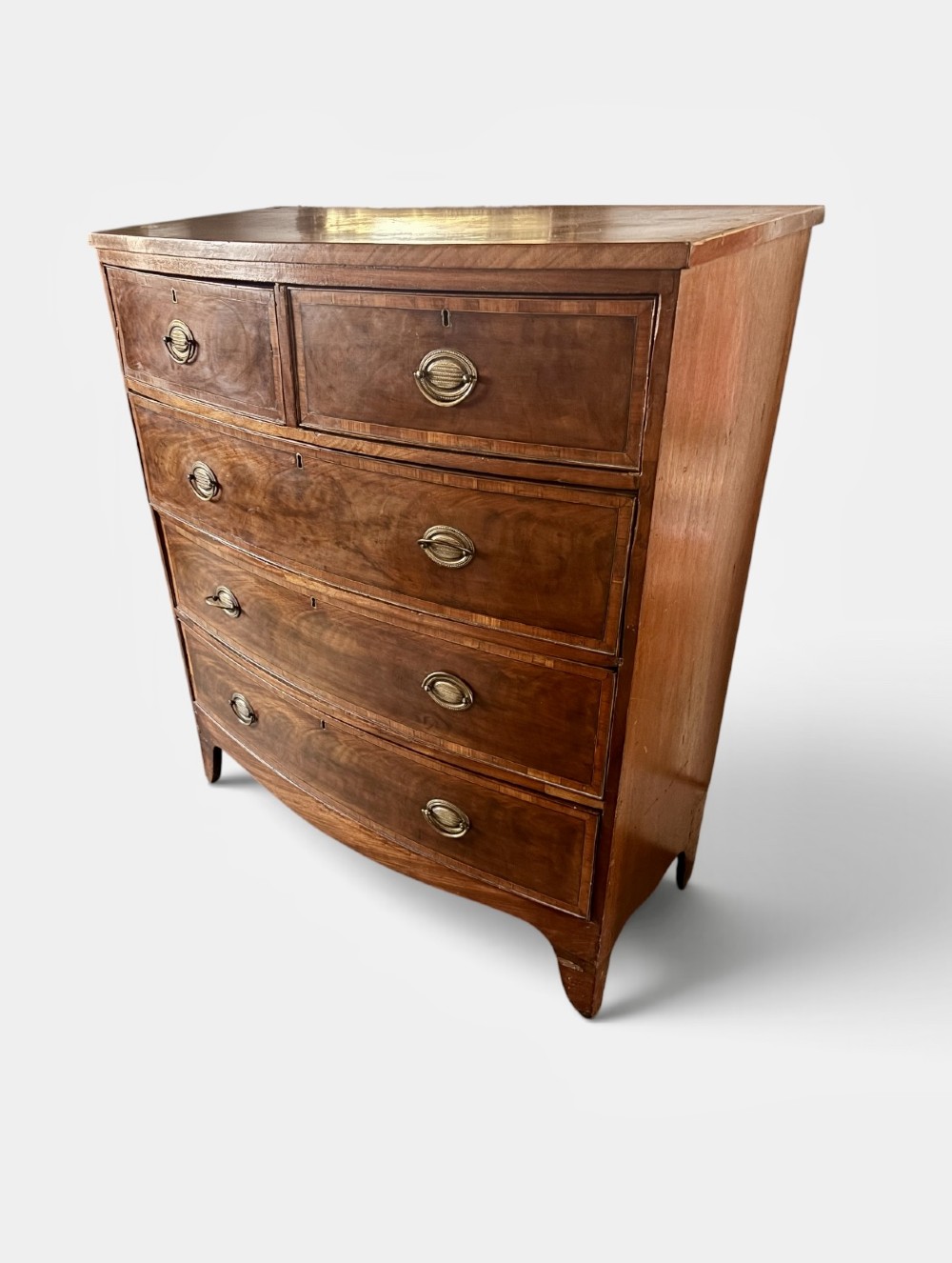 A Regency mahogany bowfront chest of drawers featuring satinwood crossbanding, brass oval handles, and splayed legs. View II