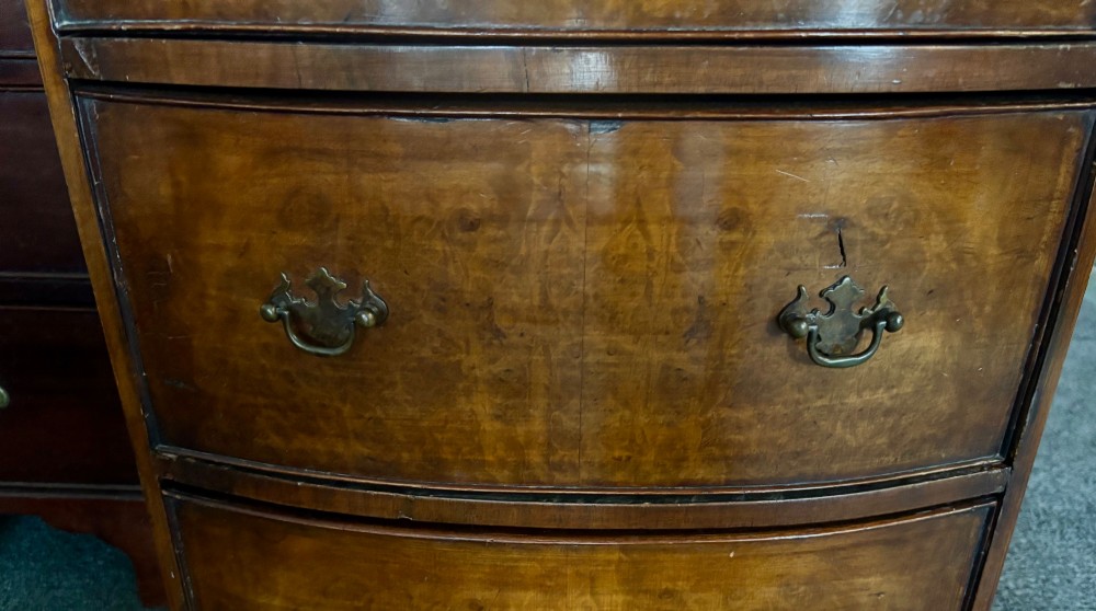An early 20th-century figured walnut bow-front tallboy featuring six stacked drawers with brass bail handles and bracket feet. View VII
