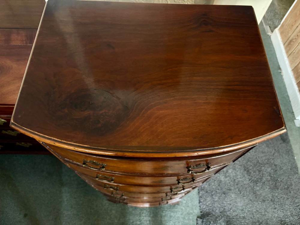 An early 20th-century figured walnut bow-front tallboy featuring six stacked drawers with brass bail handles and bracket feet. View VIII