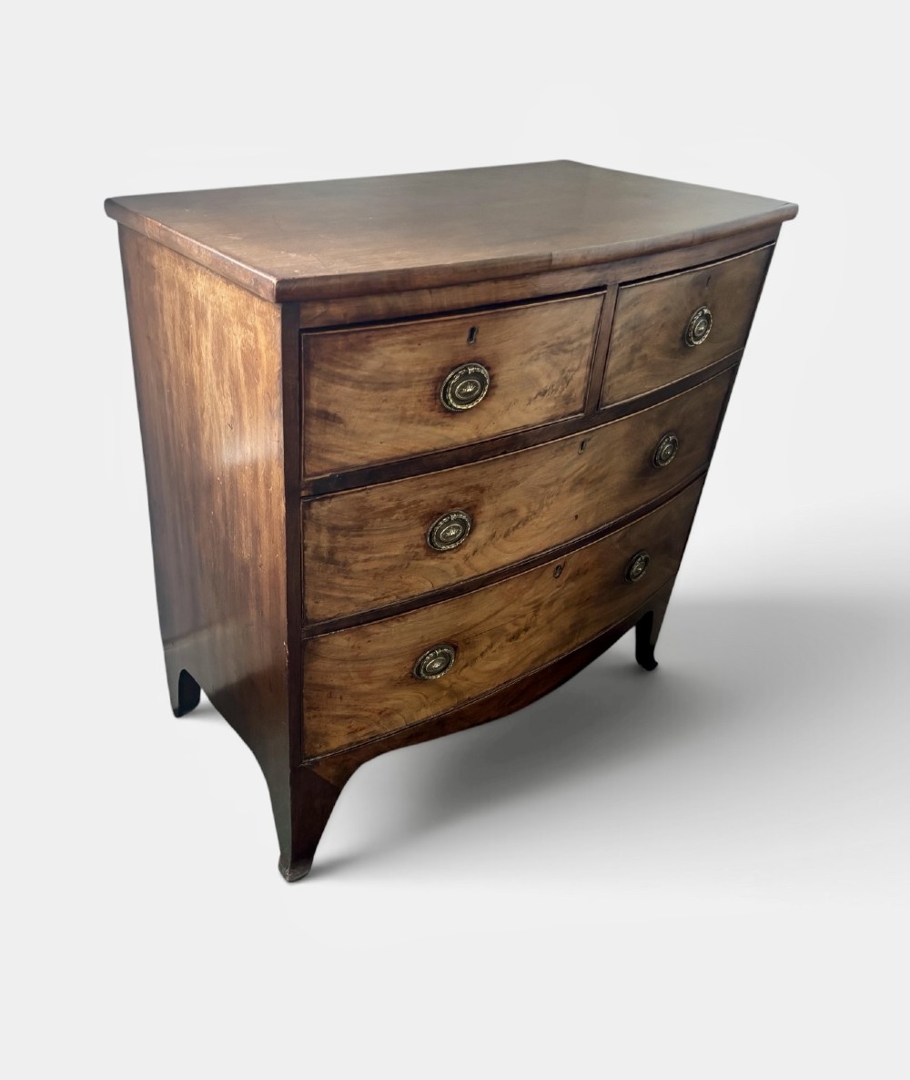 A Regency mahogany bowfront chest of drawers featuring two short drawers over two long drawers with brass ring handles and splayed feet. View II