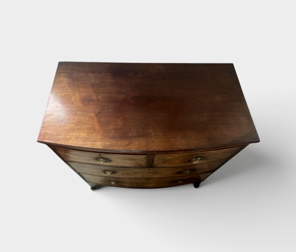 A Regency mahogany bowfront chest of drawers featuring two short drawers over two long drawers with brass ring handles and splayed feet. View IV