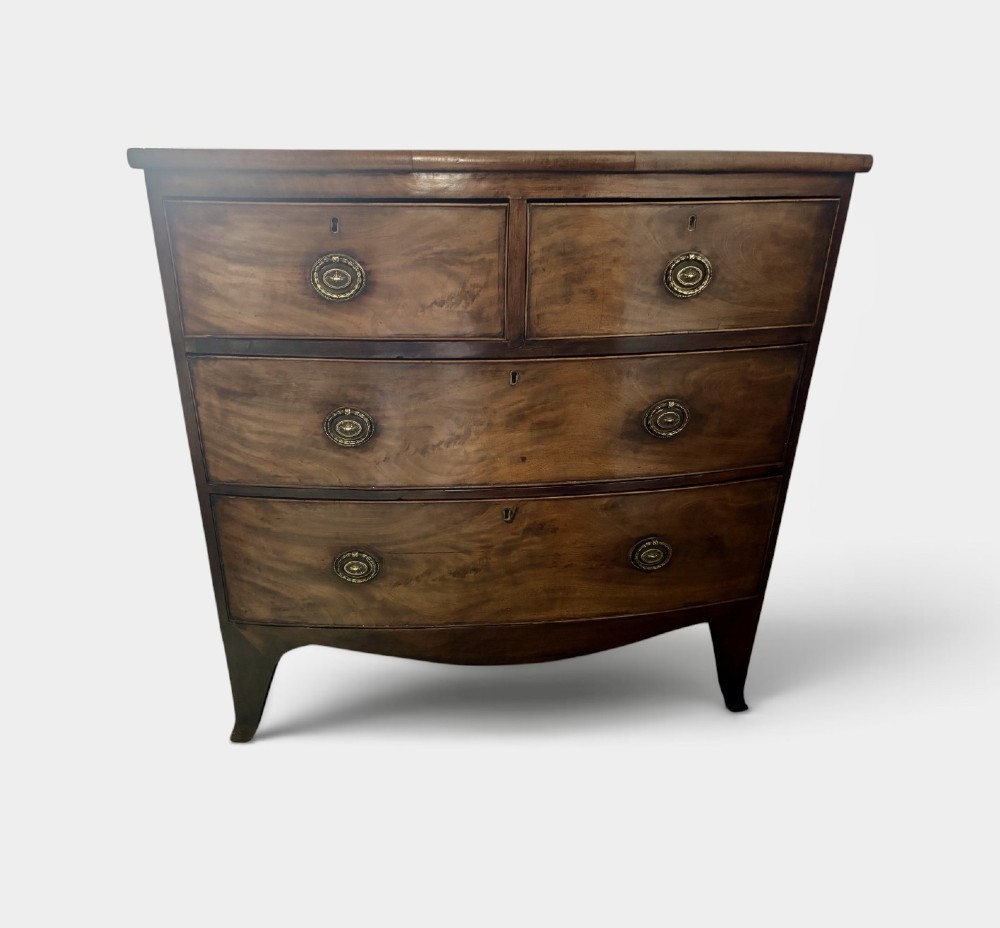 A Regency mahogany bowfront chest of drawers featuring two short drawers over two long drawers with brass ring handles and splayed feet. View V