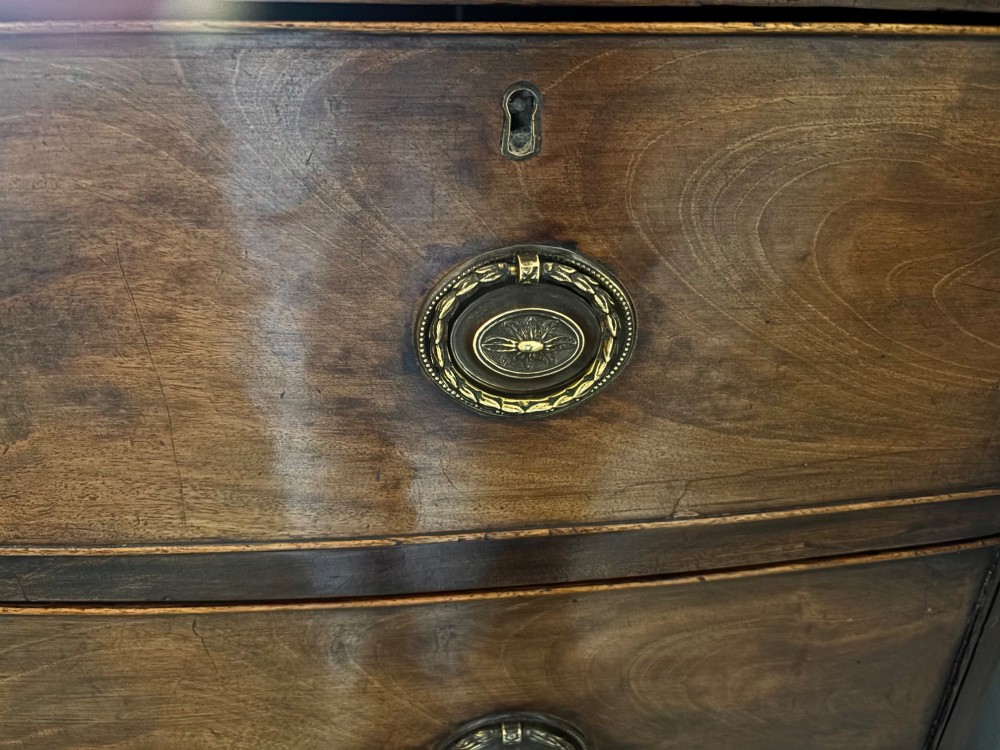 A Regency mahogany bowfront chest of drawers featuring two short drawers over two long drawers with brass ring handles and splayed feet. View VI