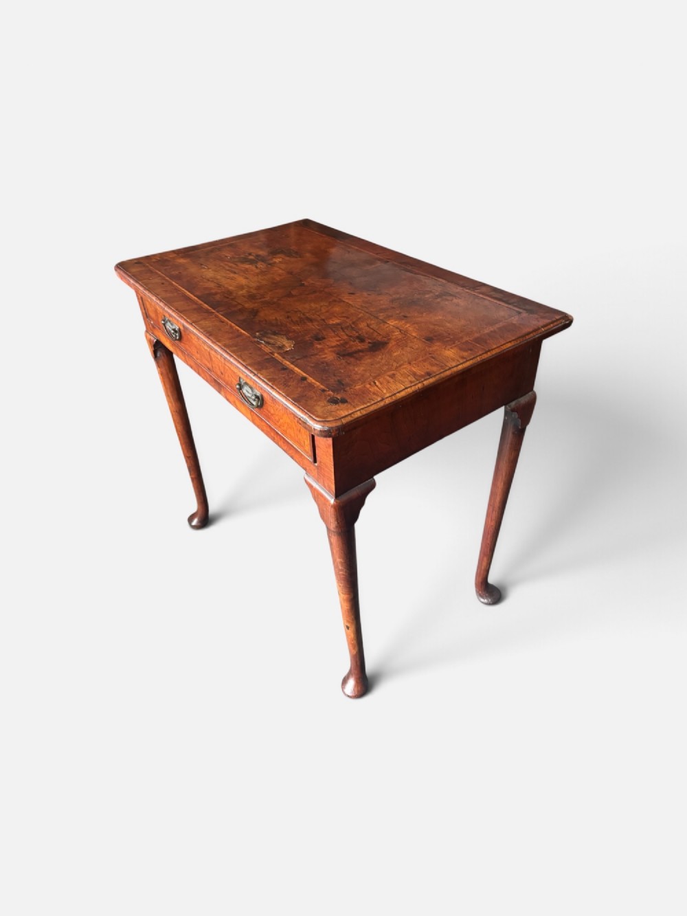A George III walnut lowboy featuring a crossbanded top, a drawer with brass handles, and slender cabriole legs terminating in pad feet.