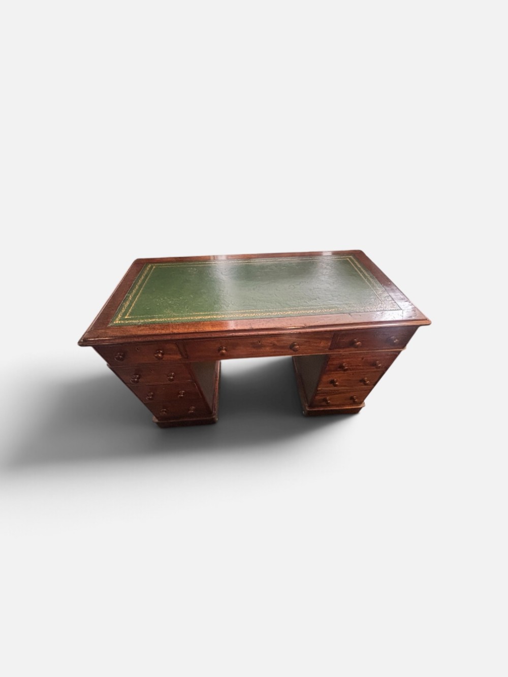 A Victorian mahogany pedestal desk featuring a green gilt-tooled leather writing surface, nine drawers with turned wooden knobs, and a central kneehole.