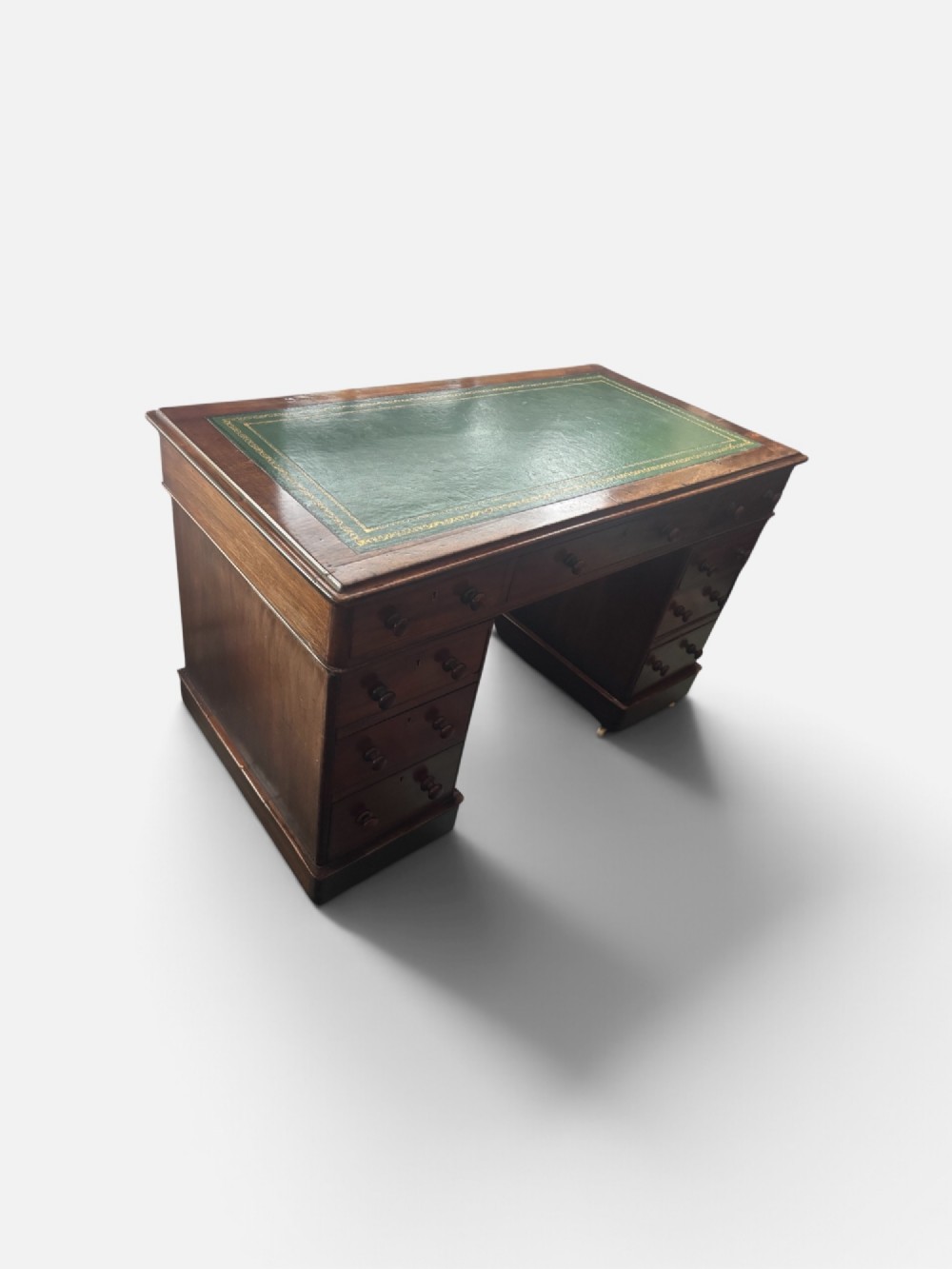 A Victorian mahogany pedestal desk featuring a green gilt-tooled leather writing surface, nine drawers with turned wooden knobs, and a central kneehole. View VII