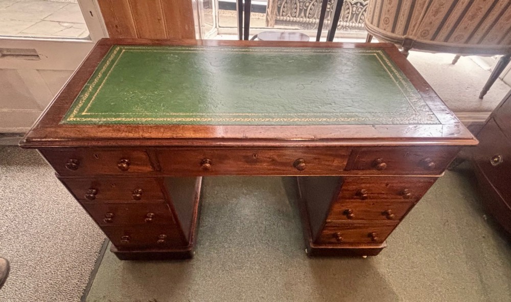 A Victorian mahogany pedestal desk featuring a green gilt-tooled leather writing surface, nine drawers with turned wooden knobs, and a central kneehole. View VIII