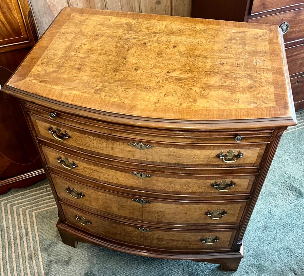 A burr walnut bow-front chest of four graduated drawers featuring brass drop handles, herringbone crossbanding, and bracket feet.