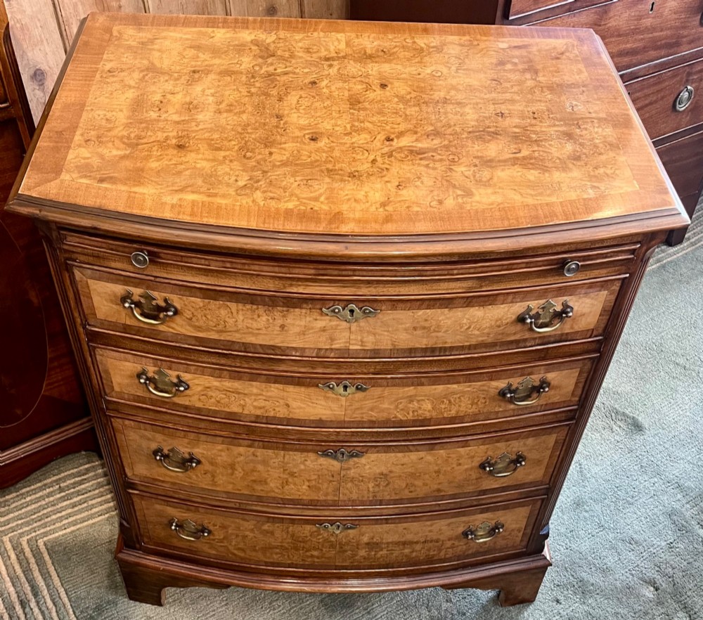 A burr walnut bow-front chest of four graduated drawers featuring brass drop handles, herringbone crossbanding, and bracket feet. View II