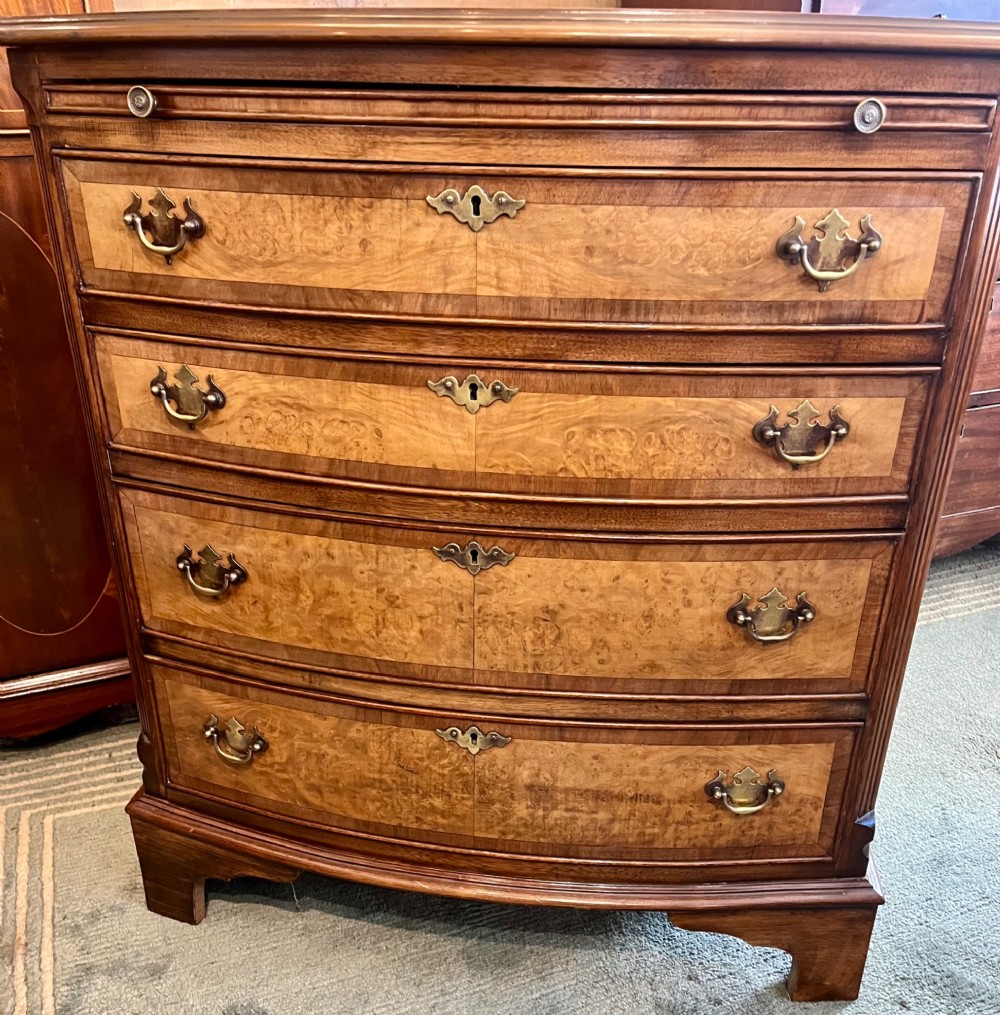 A burr walnut bow-front chest of four graduated drawers featuring brass drop handles, herringbone crossbanding, and bracket feet. View III