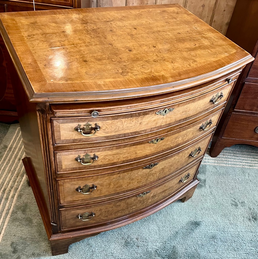 A burr walnut bow-front chest of four graduated drawers featuring brass drop handles, herringbone crossbanding, and bracket feet. View IV