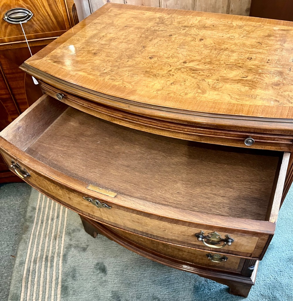 A burr walnut bow-front chest of four graduated drawers featuring brass drop handles, herringbone crossbanding, and bracket feet. View VI