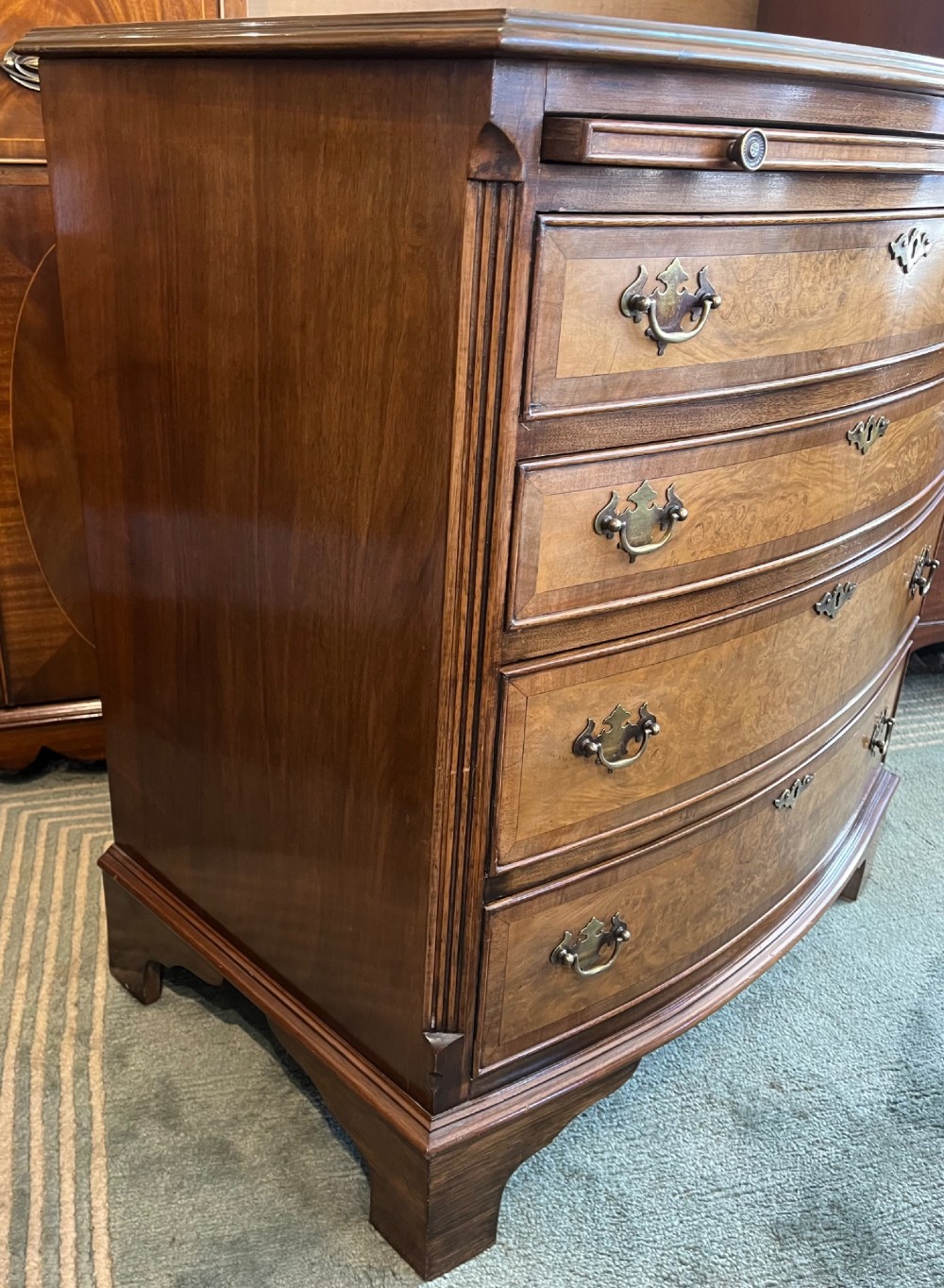 A burr walnut bow-front chest of four graduated drawers featuring brass drop handles, herringbone crossbanding, and bracket feet. View VII